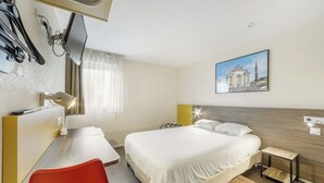 Une chambre d’hôtel comprenant un lit, un bureau, une chaise, une petite table, un téléviseur fixé au mur et un tableau.