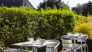 Une terrasse extérieure avec des tables et des chaises en métal, entourée d’une végétation luxuriante.