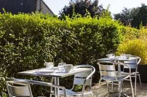 Un patio exterior con mesas y sillas de metal, rodeado de abundante vegetación.