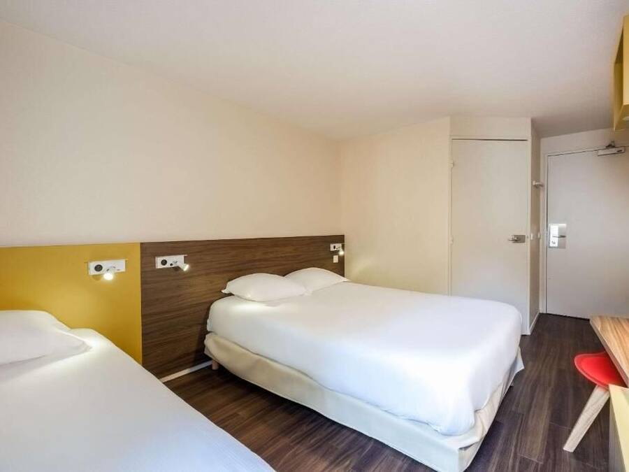 Une chambre d’hôtel avec deux lits, une tête de lit en bois, un petit bureau avec une chaise et une porte.