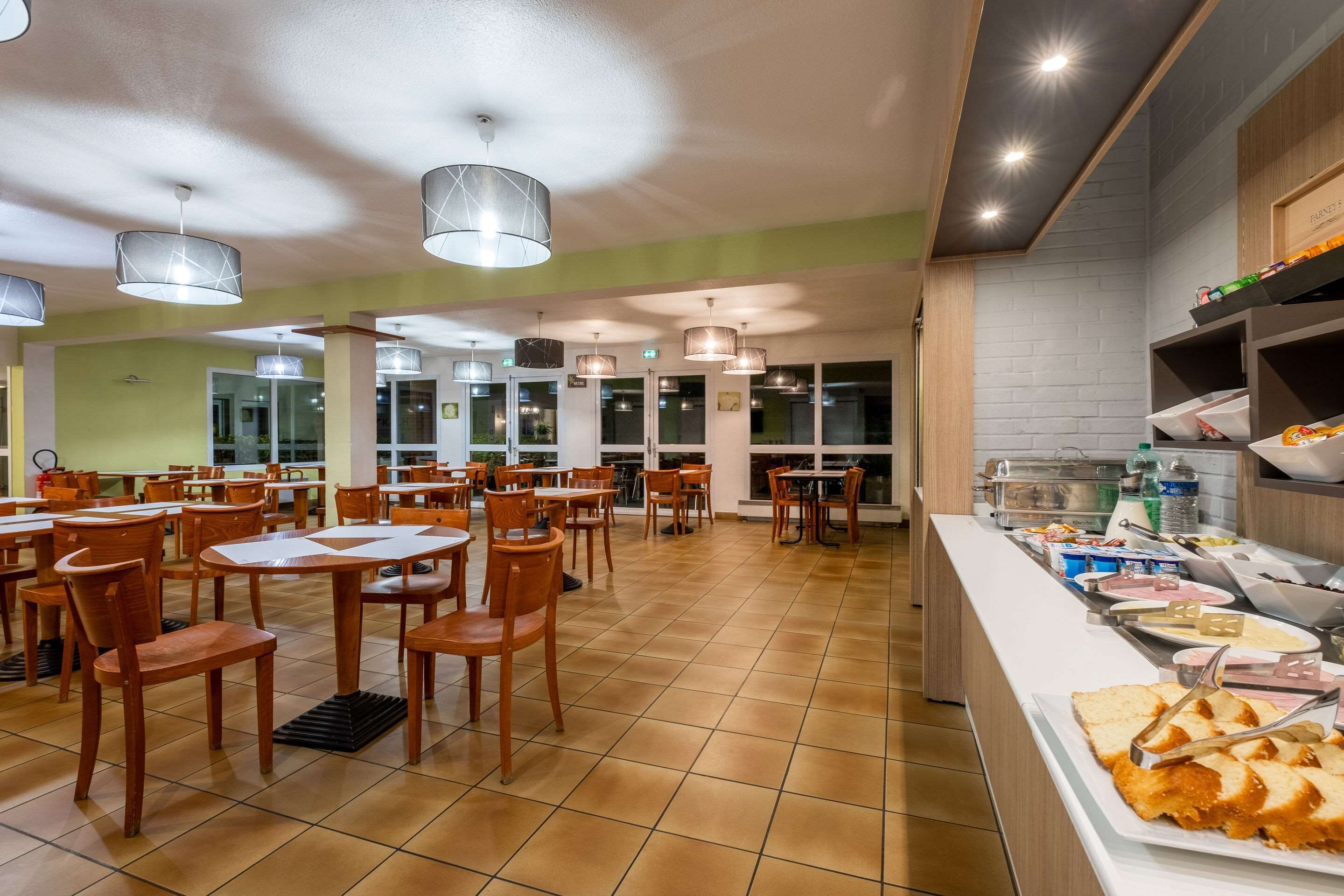 A spacious dining area with multiple tables and chairs, a buffet counter with various food items, and a modern ceiling design.