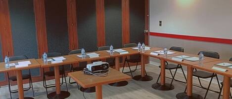 Un salón de conferencias con una larga mesa, sillas, botellas de agua, documentos, un proyector y un reloj en la pared.