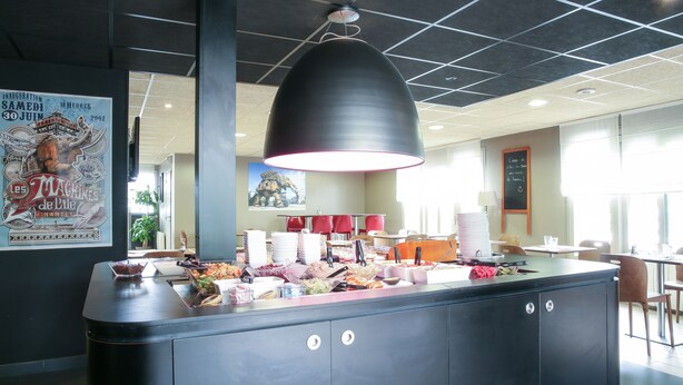 A buffet area with a variety of food items, a large black pendant light, and a poster on the wall. - Hôtel Inn Design Laval  (Laval)