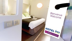 A hotel room with a bed, a laptop, and a welcome sign. - Hôtel Inn Design Laval  (Laval)