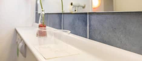 A bathroom counter with a clear glass vase containing a single flower, a mirror, and a towel rack.