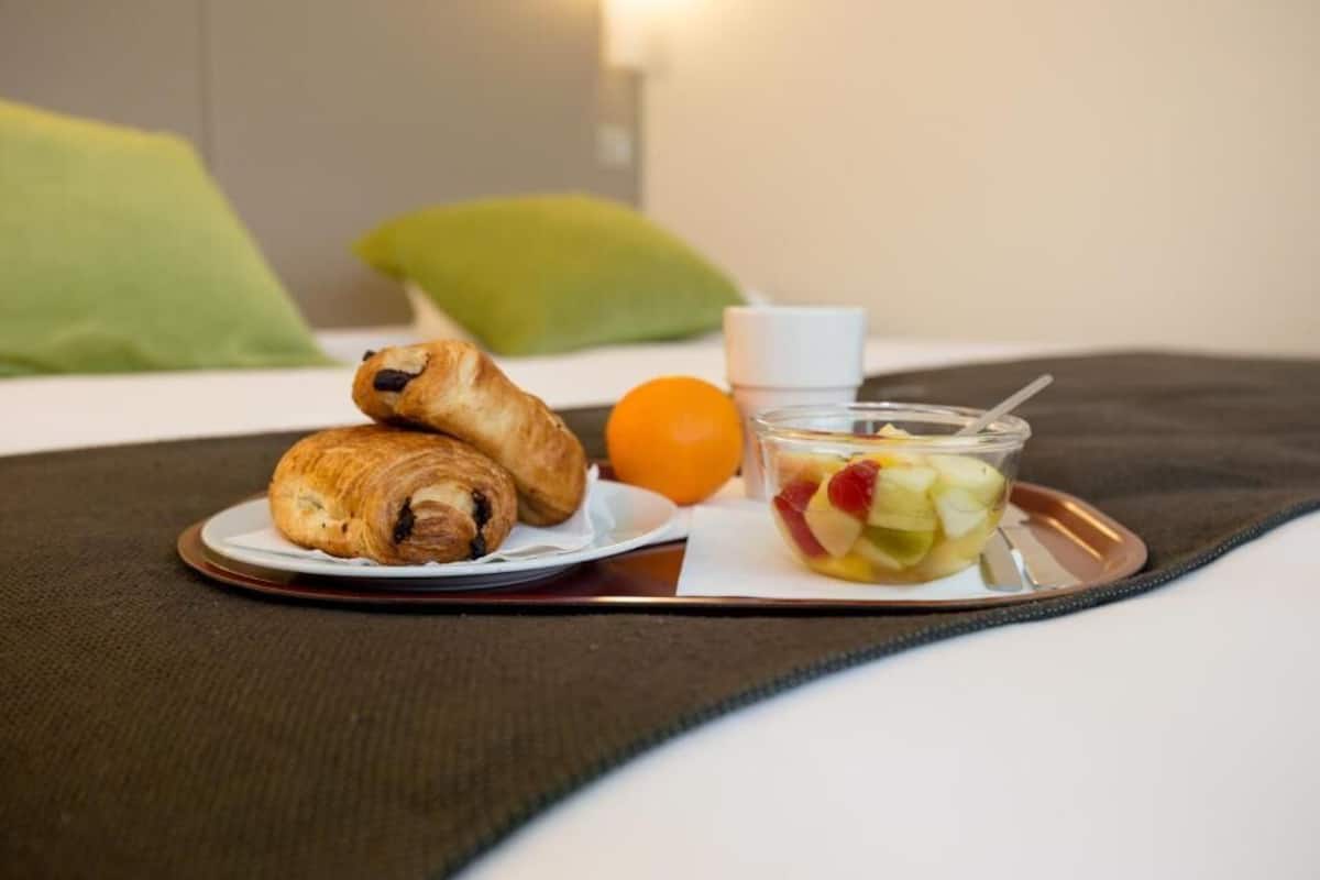 A breakfast setting with croissants, an orange, and a fruit salad on a tray.