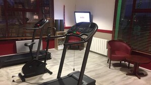 A gym with treadmills, a stationary bike, and a red chair. - Hôtel Inn Design Laval  (Laval)