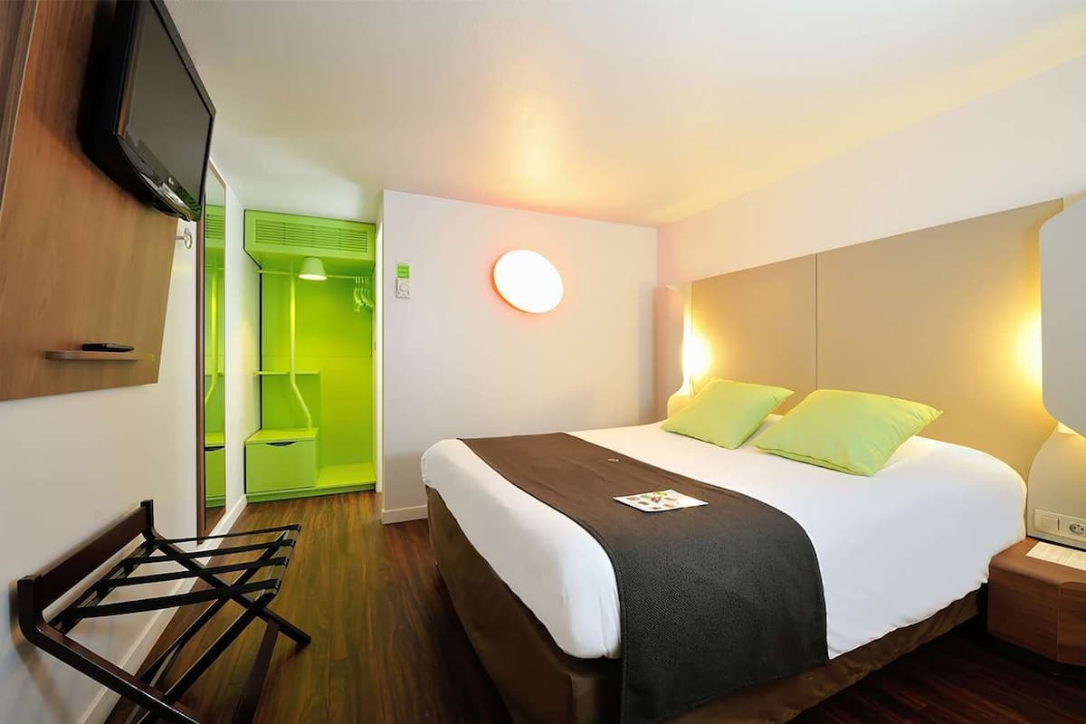 A hotel room with a bed, bedside table, and a TV mounted on the wall.