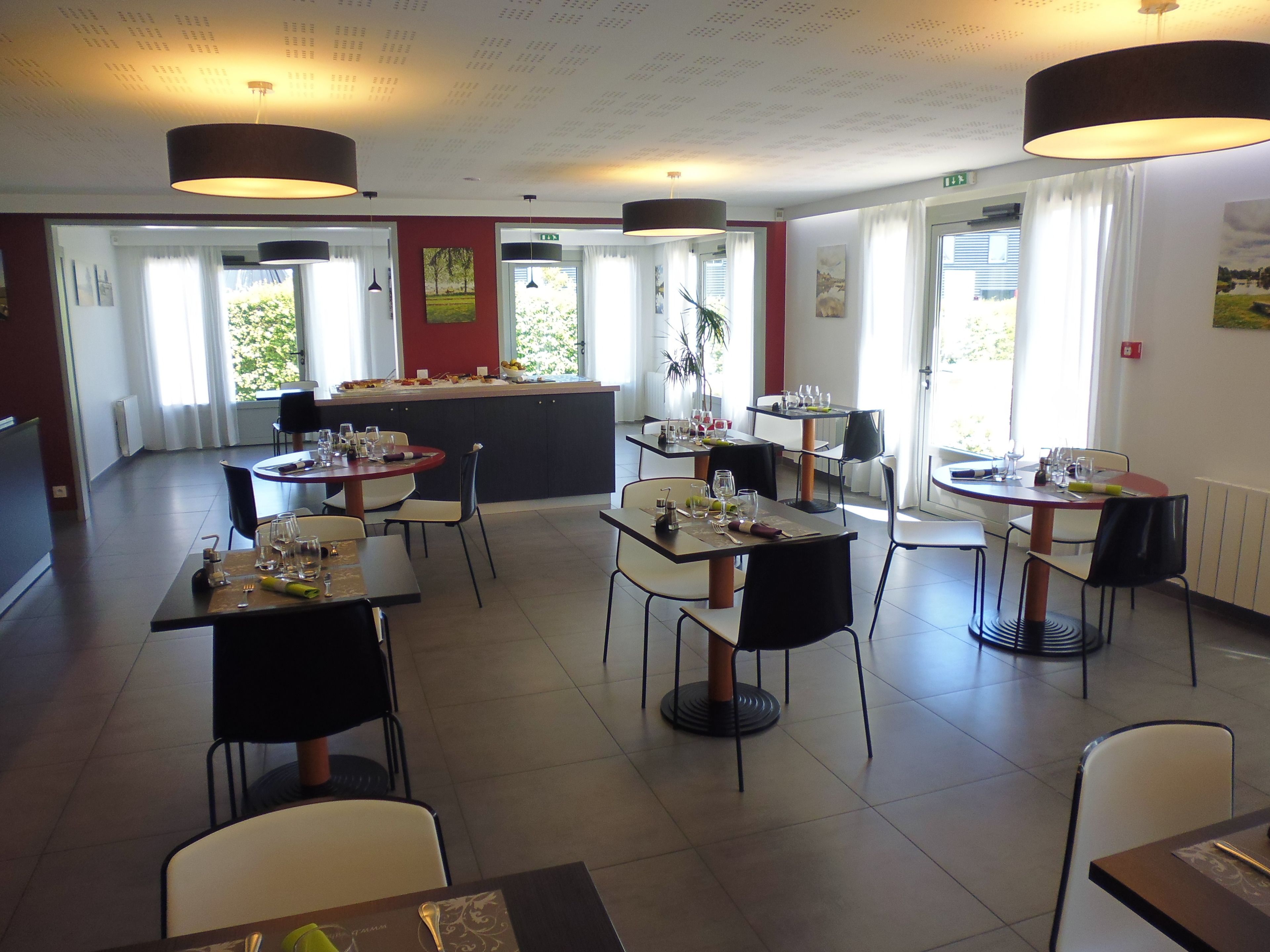 A restaurant with multiple tables and chairs, a central bar area, and large windows allowing natural light.