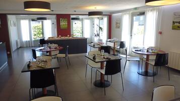 A restaurant with multiple tables and chairs, a central bar area, and large windows allowing natural light.