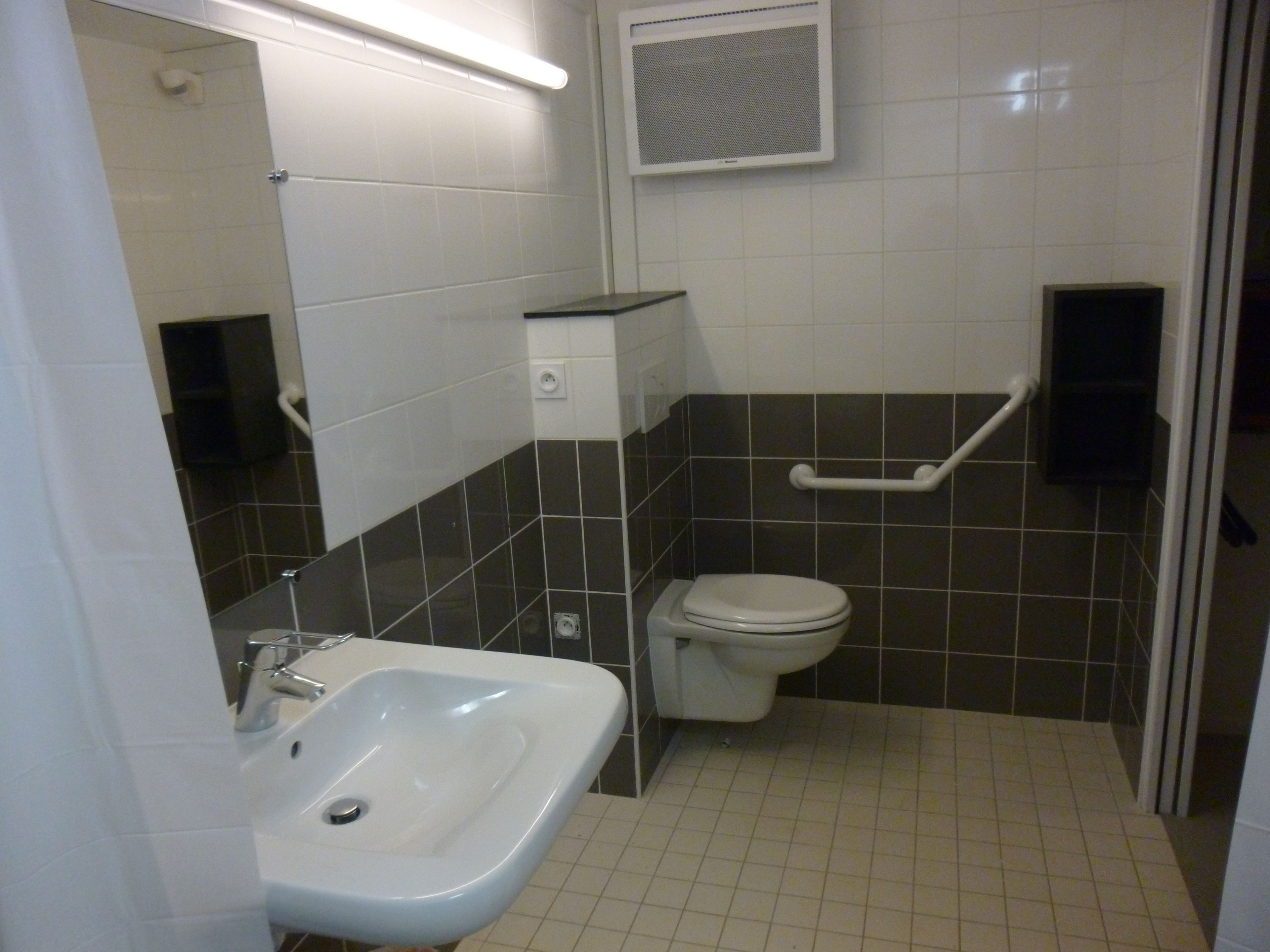 Un baño con un lavamanos blanco, un inodoro y un pasamanos.