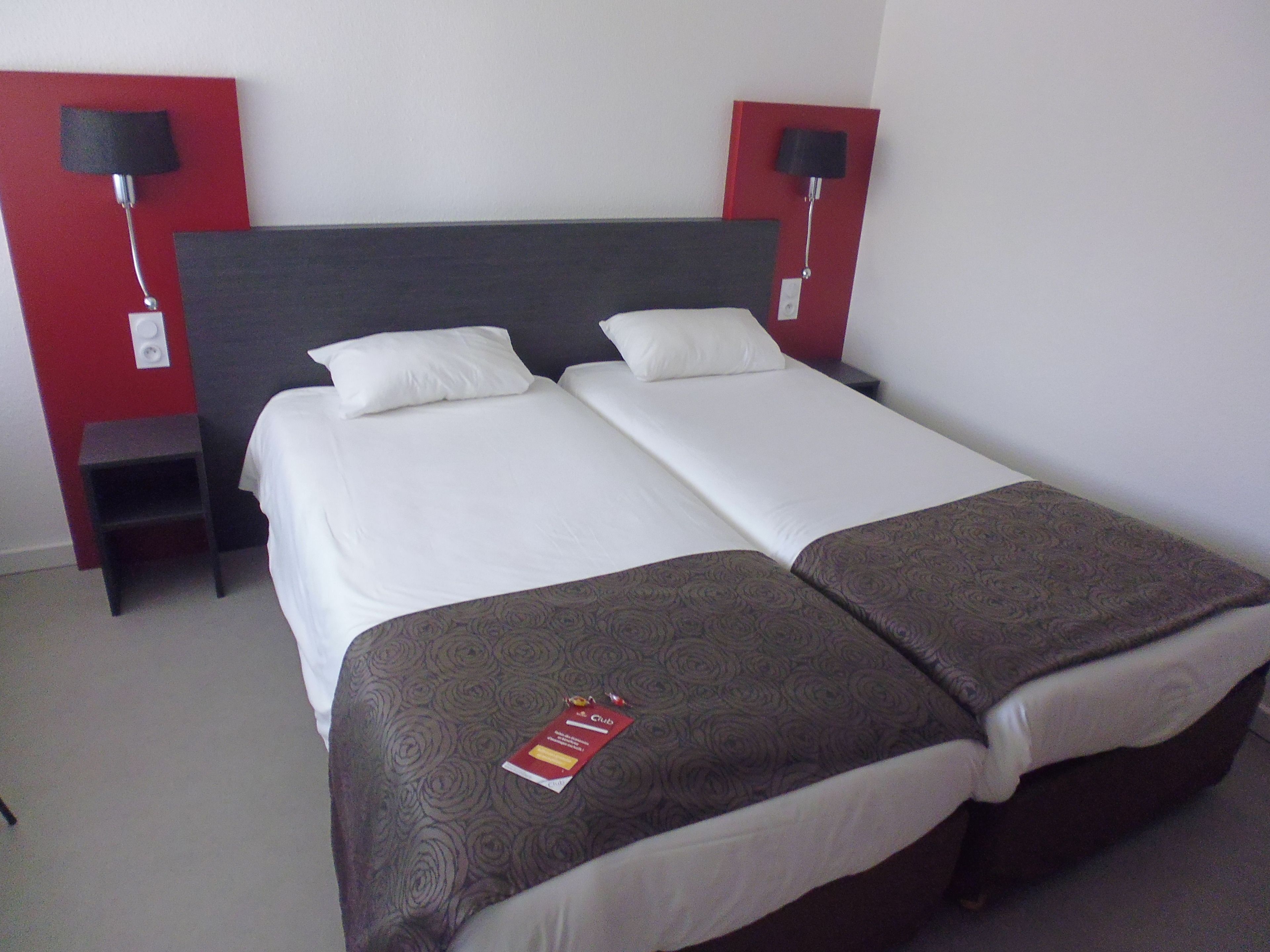 A double bed with two pillows, a bedside table, and a red wall.
