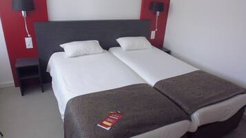 A double bed with two pillows, a bedside table, and a red wall.