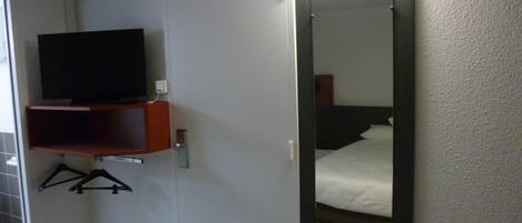 A hotel room with a bed, a television on a shelf, and a mirror.