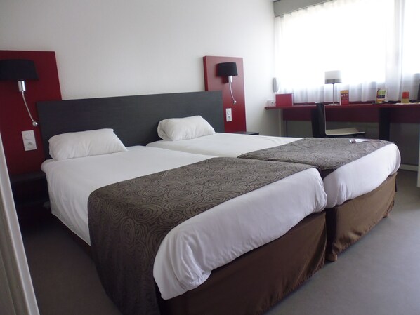 A hotel room with two beds, a desk, and a chair.