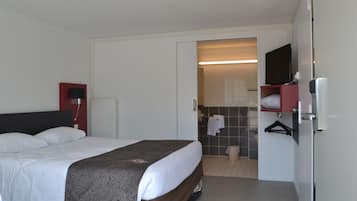 Una habitación de hotel con cama, televisión, baño con ducha y un perchero para toallas.