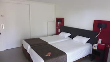 A double bed with a patterned bedspread, a white bedside table with a lamp, and a red accent wall.