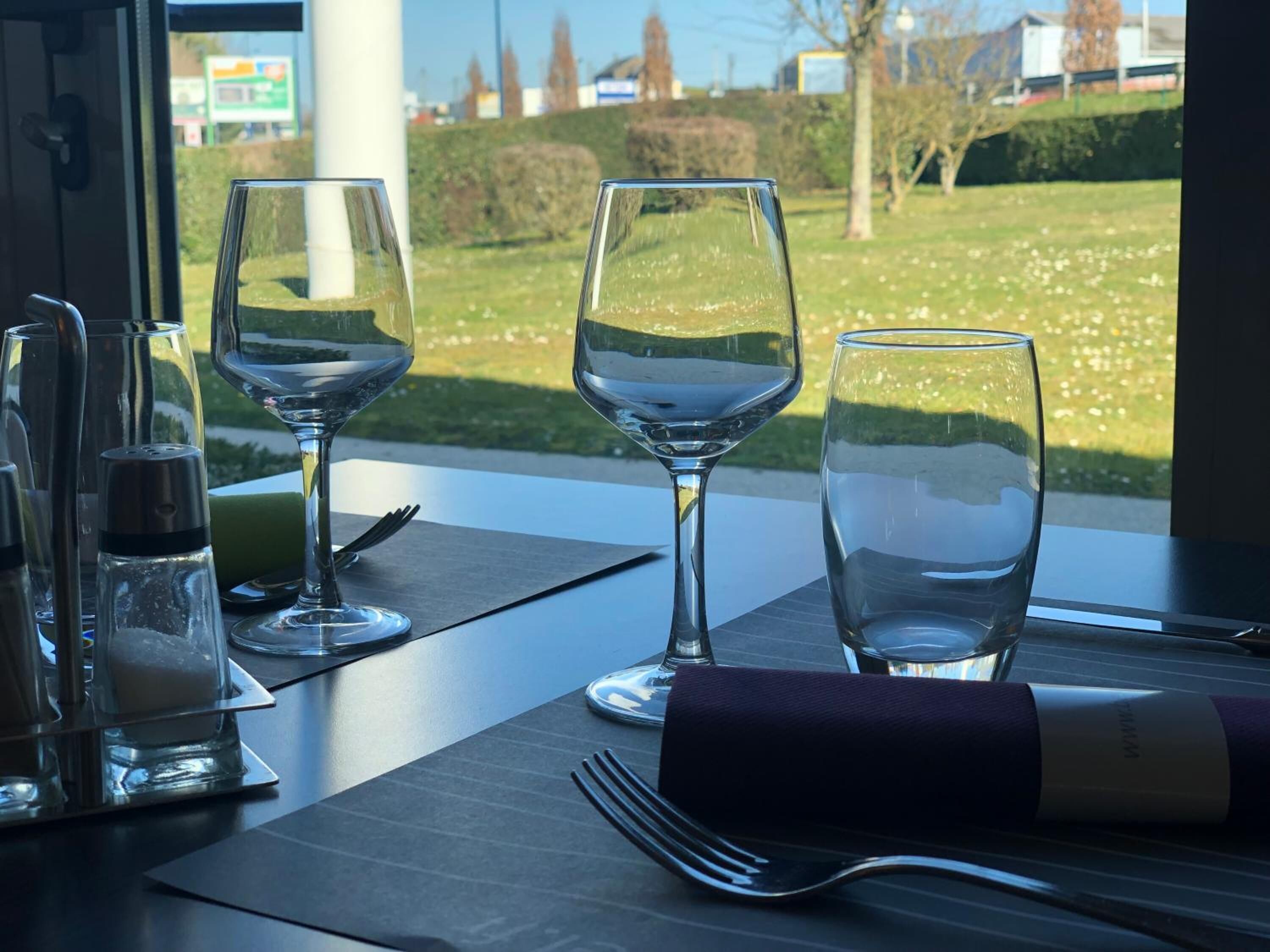 A dining table with three wine glasses, a salt and pepper shaker, and a fork on a dark placemat.