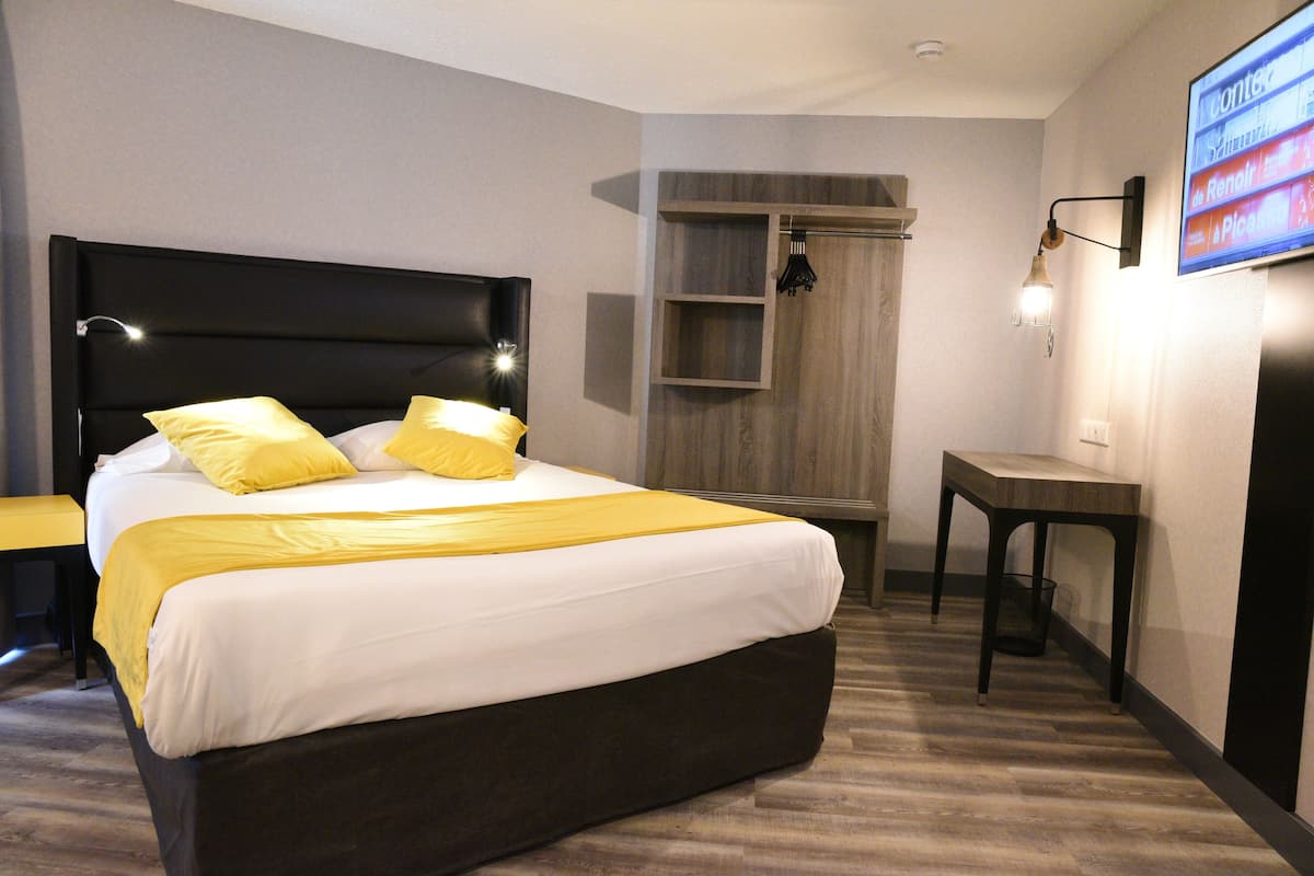 Une chambre d’hôtel moderne avec un grand lit, une table de chevet, un téléviseur fixé au mur et une armoire intégrée.
