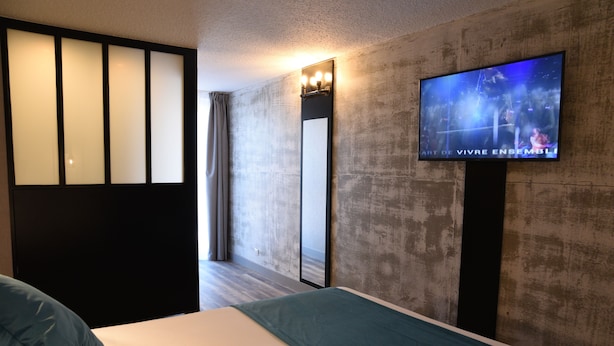A hotel room with a bed, a TV mounted on the wall, a large mirror, and a sliding door. - The Originals Boutique, Hôtel Montélimar (Montélimar)