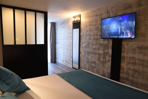 A hotel room with a bed, a TV mounted on the wall, a large mirror, and a sliding door. - The Originals Boutique, Hôtel Montélimar (Montélimar)