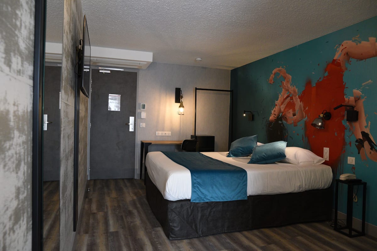 Une chambre d’hôtel moderne, équipée d’un lit, d’un bureau et ornée d’une grande fresque murale.