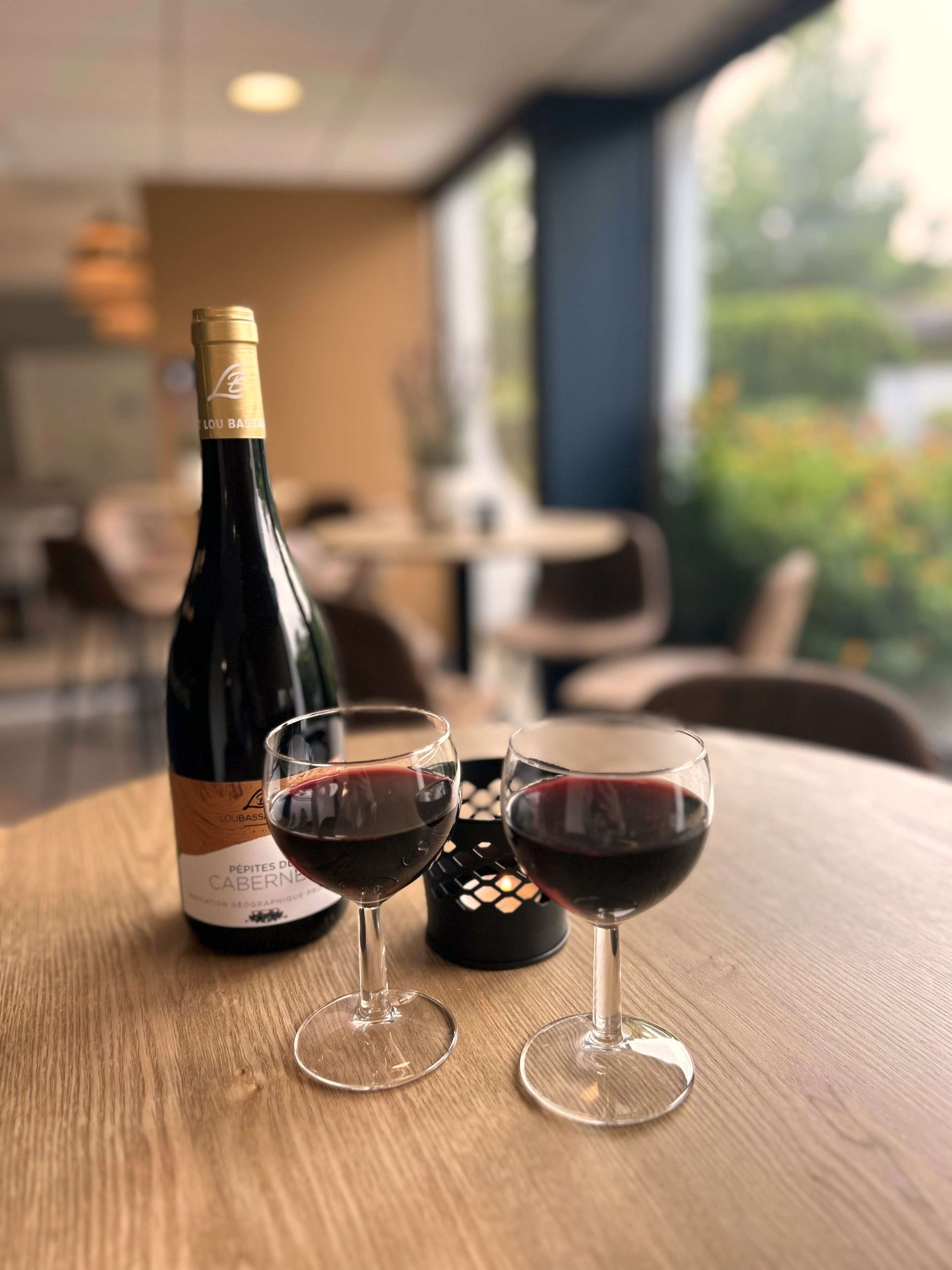 A bottle of wine and two glasses on a wooden table in a restaurant setting.
