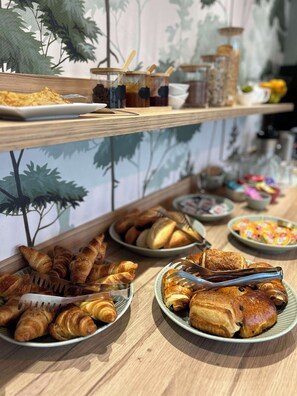 Una mesa de buffet con diversos alimentos, incluyendo croissants, pasteles y una selección de bebidas.