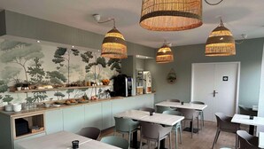 Un caffè moderno con tavoli e sedie in legno, un bancone con diversi articoli e tre grandi lampade a sospensione in vimini.