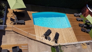 Una piscina sul tetto con terrazza in legno, lettini e un ombrellone verde.
