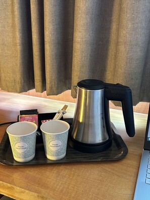 Una cafetera sobre una bandeja con dos tazas decoradas y una tarjeta.