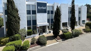 Un edificio moderno con el nombre 'Kyriad' bien visible. Presenta una fachada simétrica con ventanales amplios y una entrada central.
