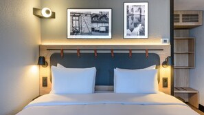 A neatly made bed with white linens, a headboard with a textured design, and two wall-mounted picture frames above it. - Campanile NATURE - Niort Est La Crèche (La Creche)