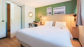 A hotel room with a large bed, a desk, a chair, and two wall-mounted lamps. - Campanile NATURE - Saint-Germain-en-Laye (Saint-Germain-en-Laye)