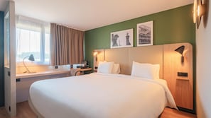 A hotel room with a large bed, a desk with a lamp, a window with curtains, and two framed pictures on the wall. - Campanile NATURE - Saint-Germain-en-Laye (Saint-Germain-en-Laye)