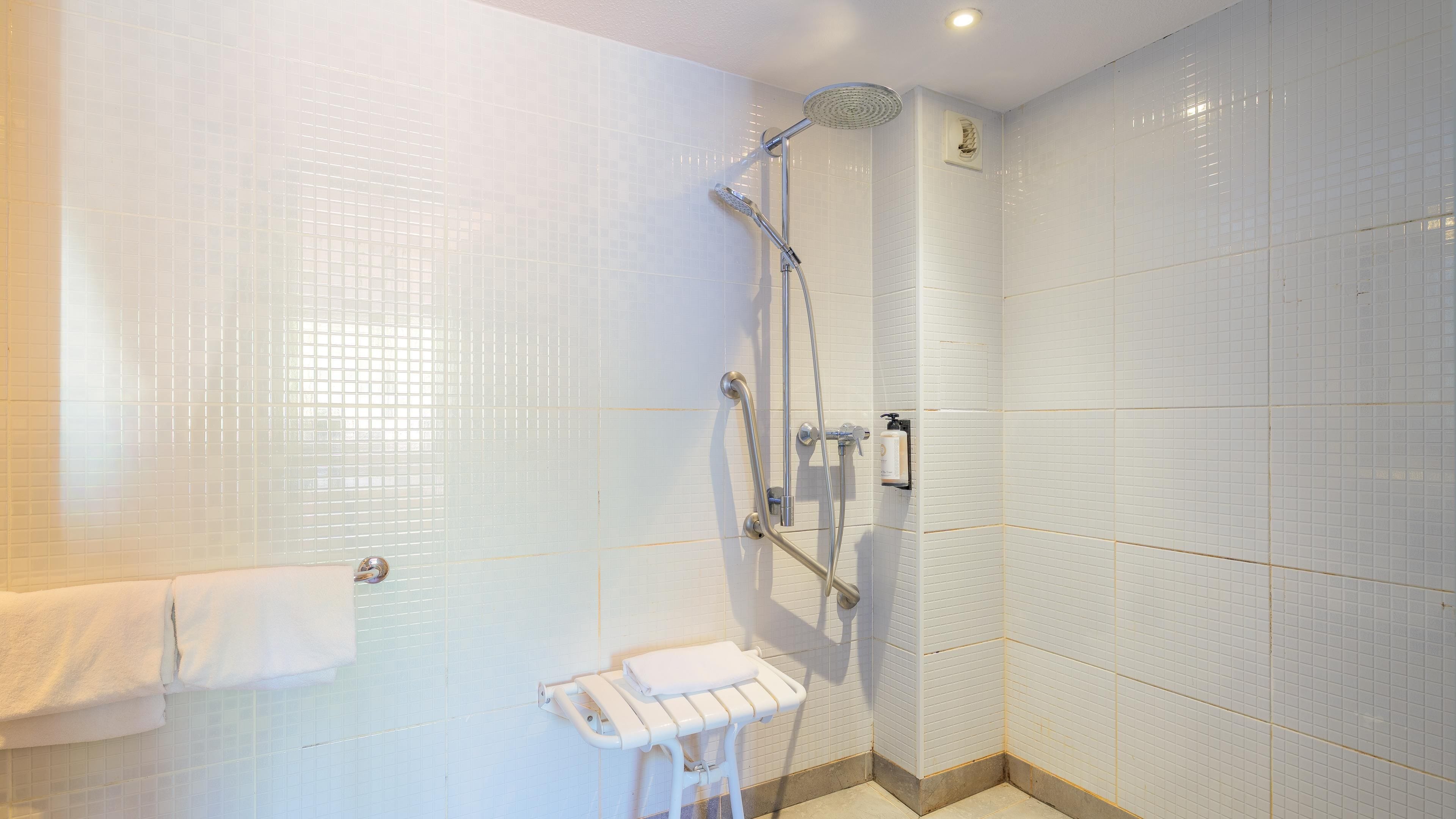 Une salle de bain moderne avec des murs carrelés de blanc, une douche avec un pommeau de douche amovible, un porte-serviettes et une bouteille de shampoing.
