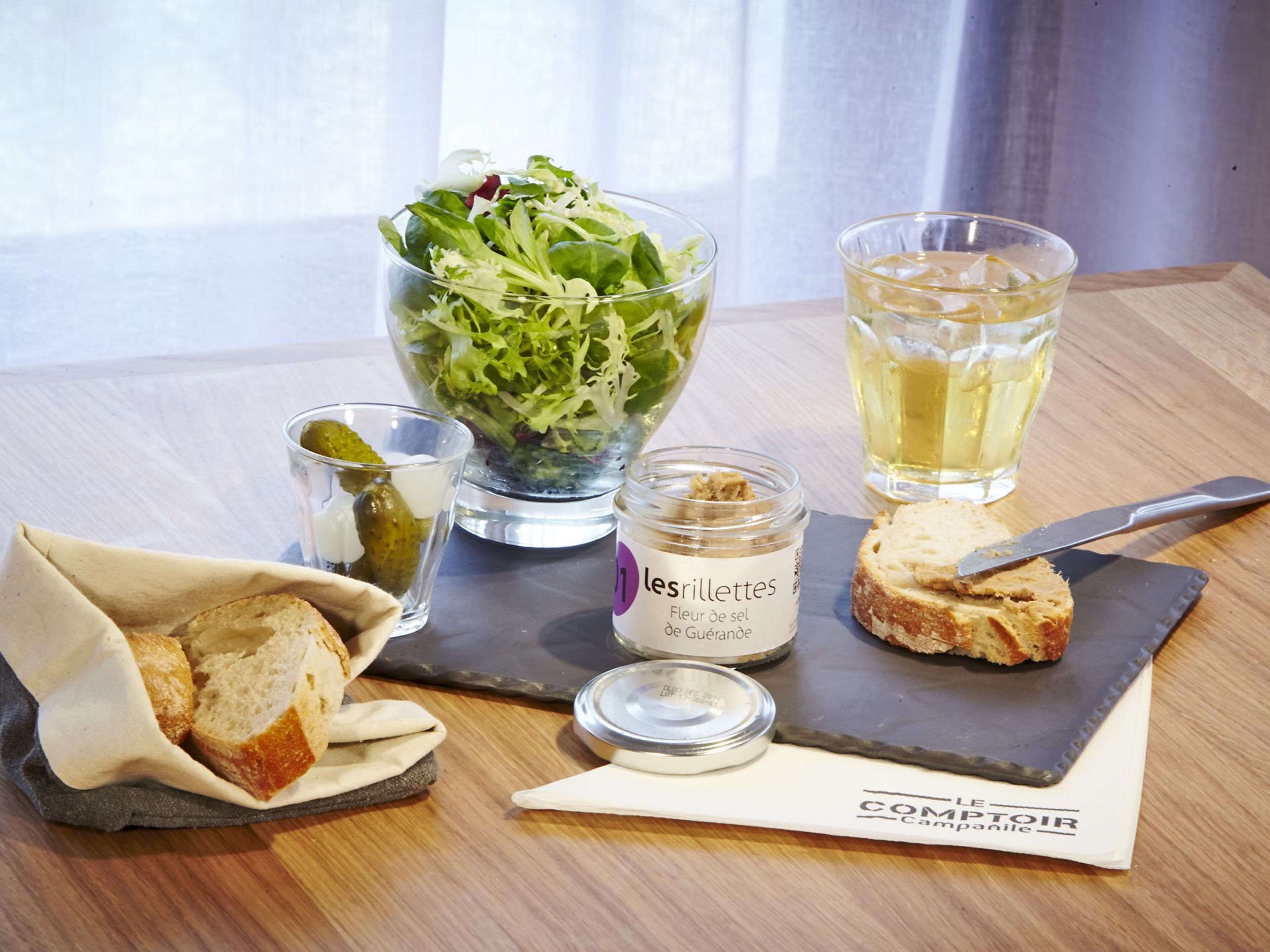 A table with a glass of water, a glass of wine, a jar of mustard, a piece of bread, and a salad.