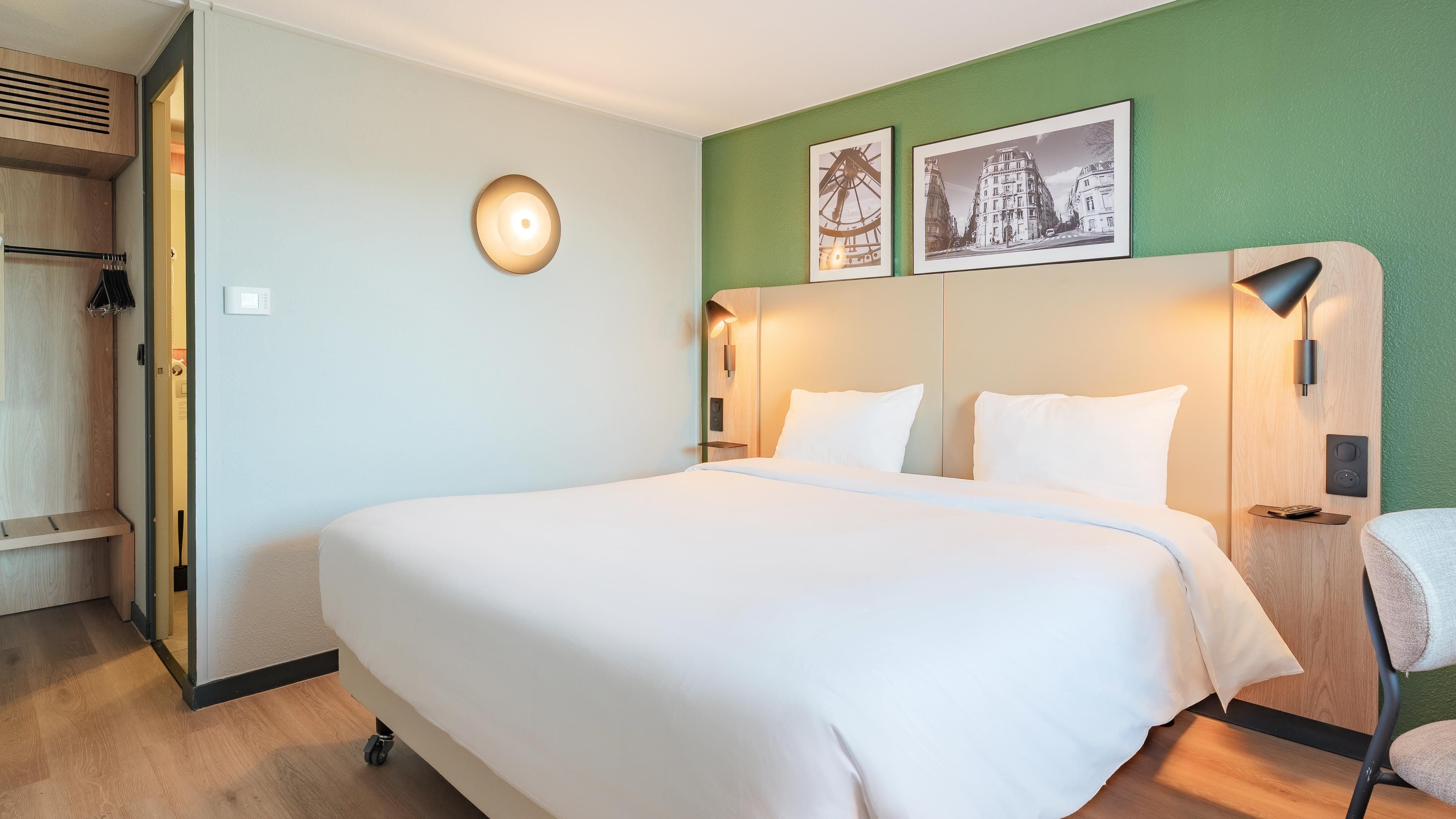 Quarto de hotel com cama grande, guarda-roupa, mesa de cabeceira e duas luminárias fixadas na parede.