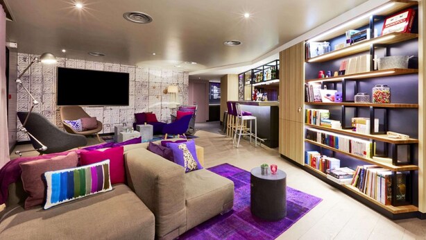 A modern living room with a sofa, armchairs, a coffee table, and a bookshelf filled with books. - Campanile NATURE - Saint-Germain-en-Laye (Saint-Germain-en-Laye)