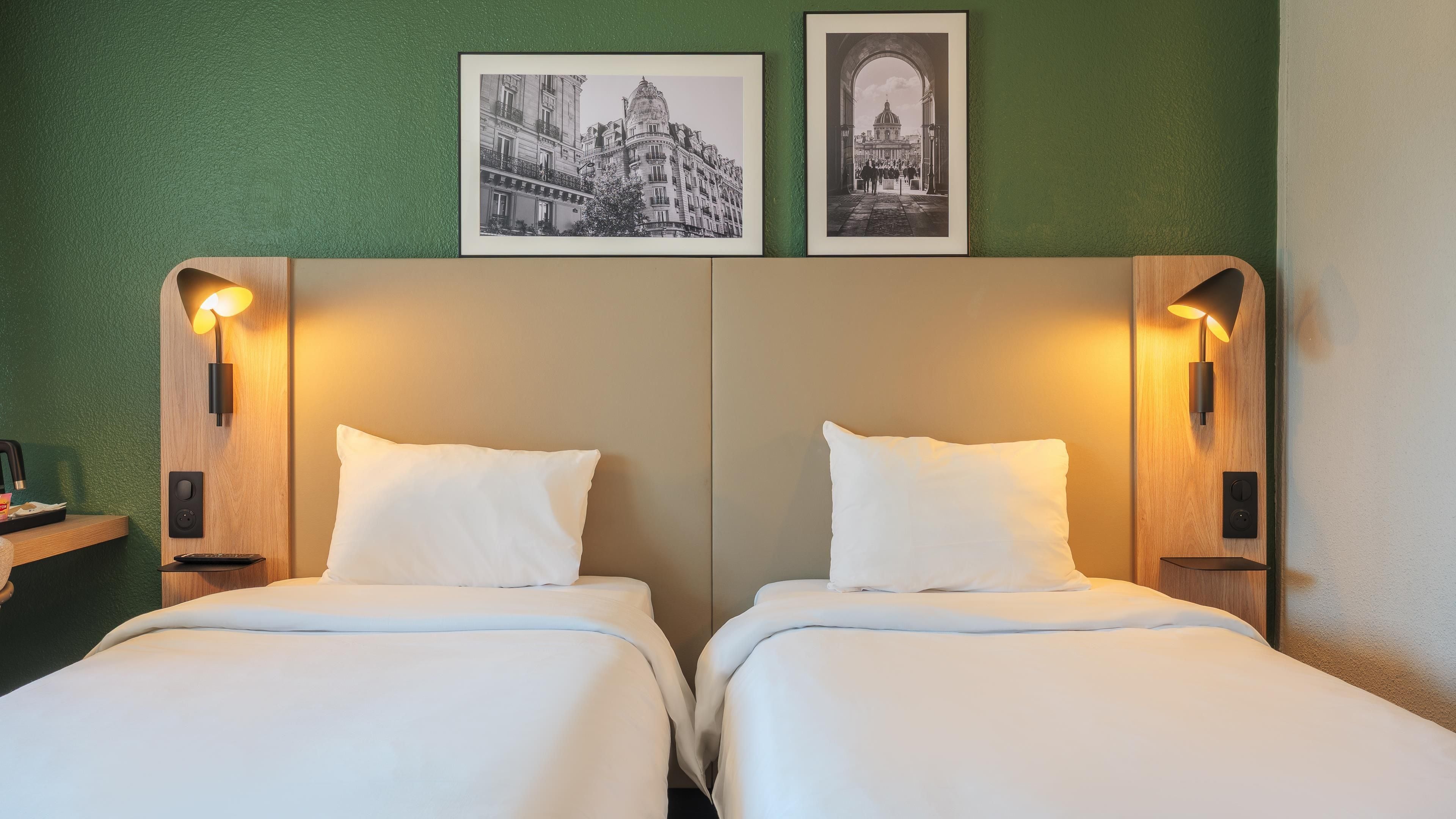 Habitación de hotel con dos camas, una pared verde y dos cuadros colgados sobre las camas.