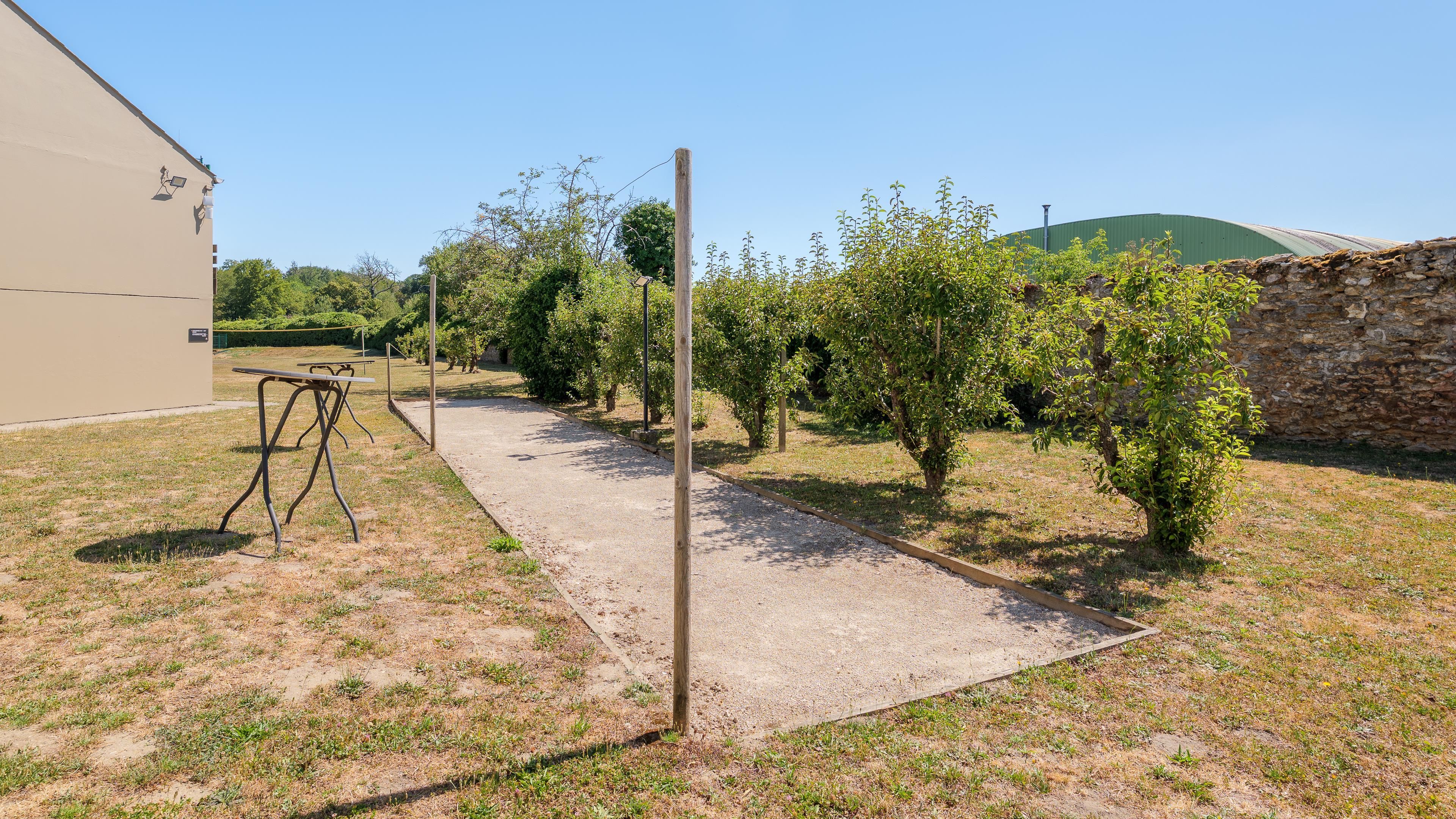 A gravel path leading through a garden with a metal table and benches, surrounded by trees and a stone wall.