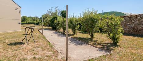 A gravel path leading through a garden with a metal table and benches, surrounded by trees and a stone wall.