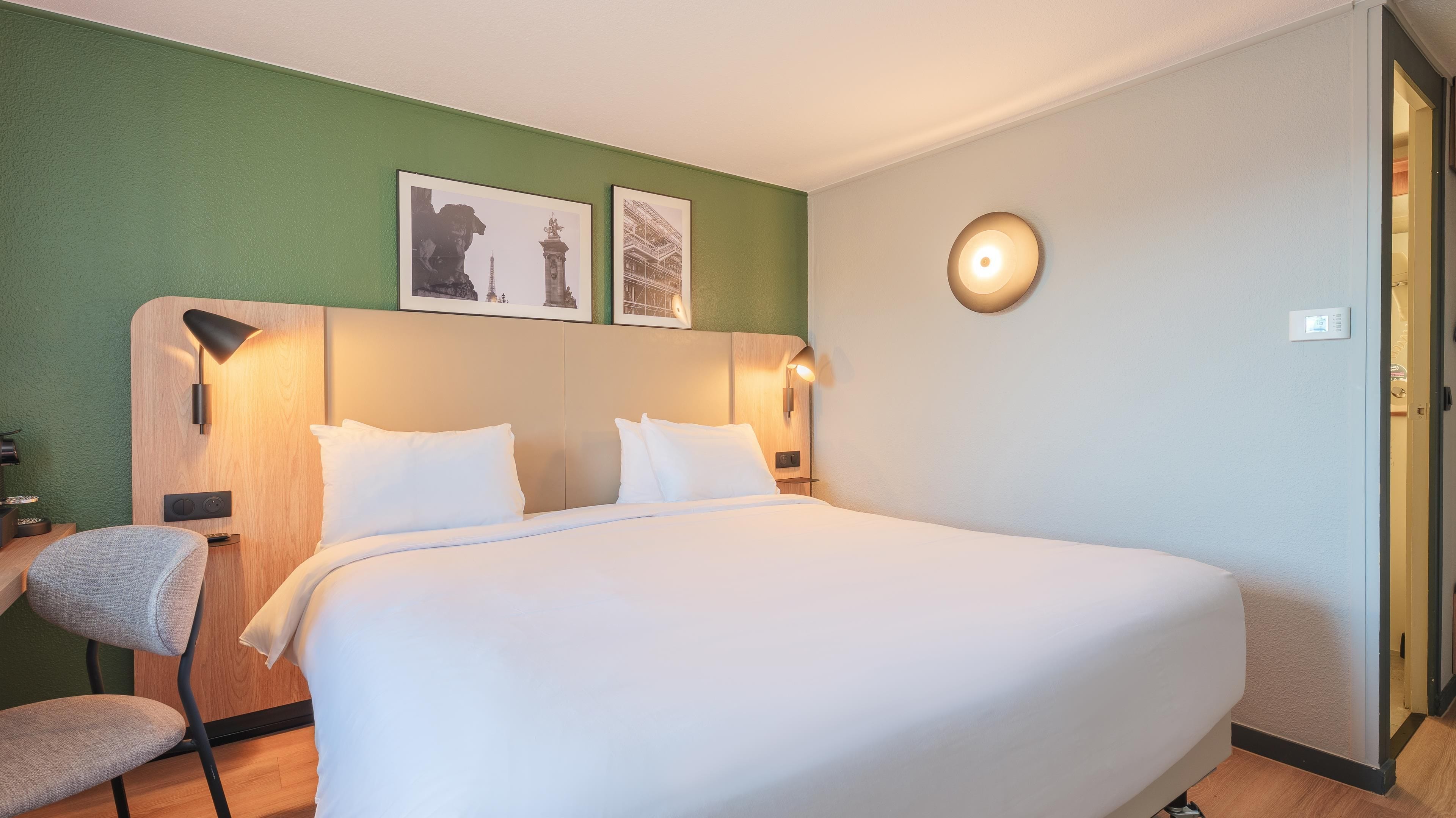 A hotel room with a large bed, two wall-mounted lamps, and two framed pictures on the wall.