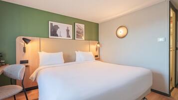 A hotel room with a large bed, two wall-mounted lamps, and two framed pictures on the wall.