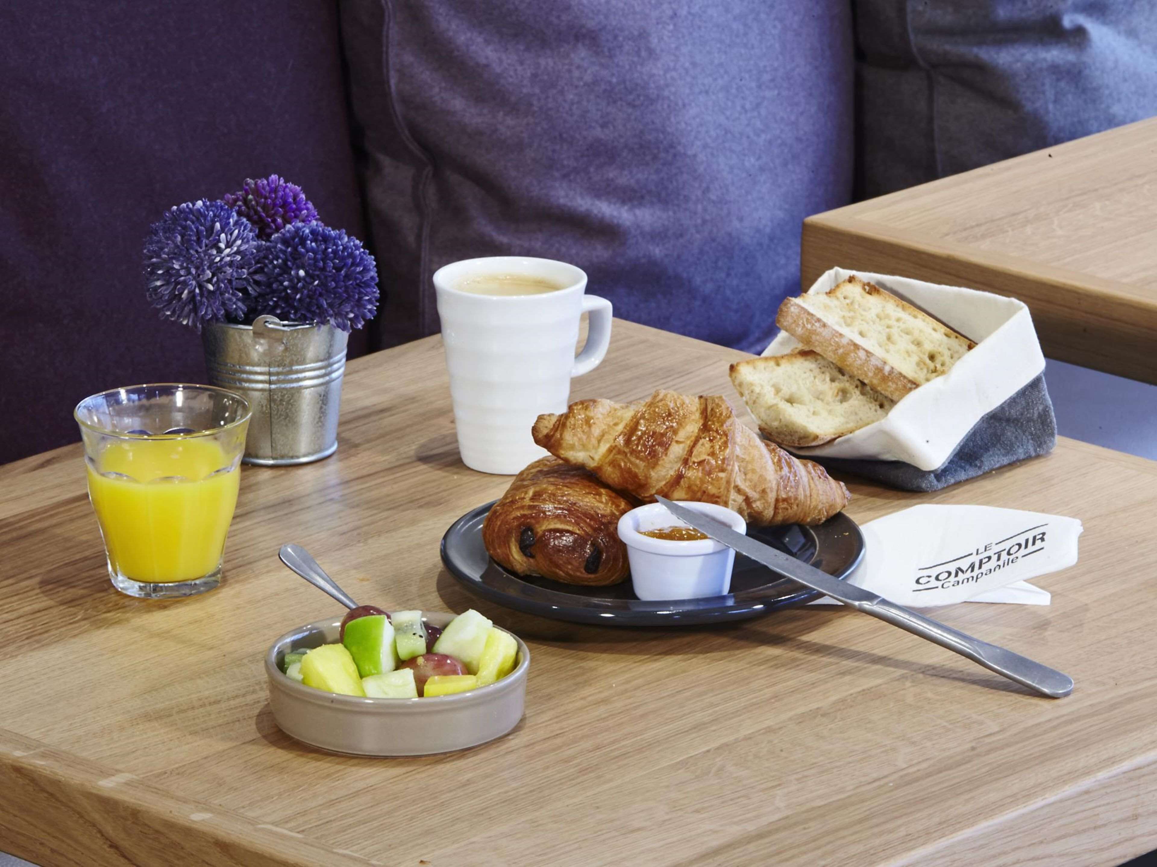 A breakfast setting with croissants, fruit, coffee, and juice on a wooden table.