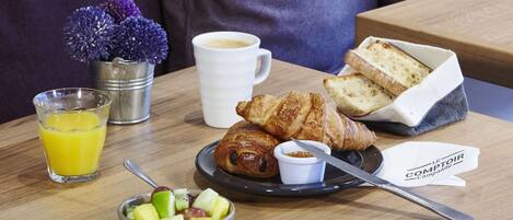 A breakfast setting with croissants, fruit, coffee, and juice on a wooden table.