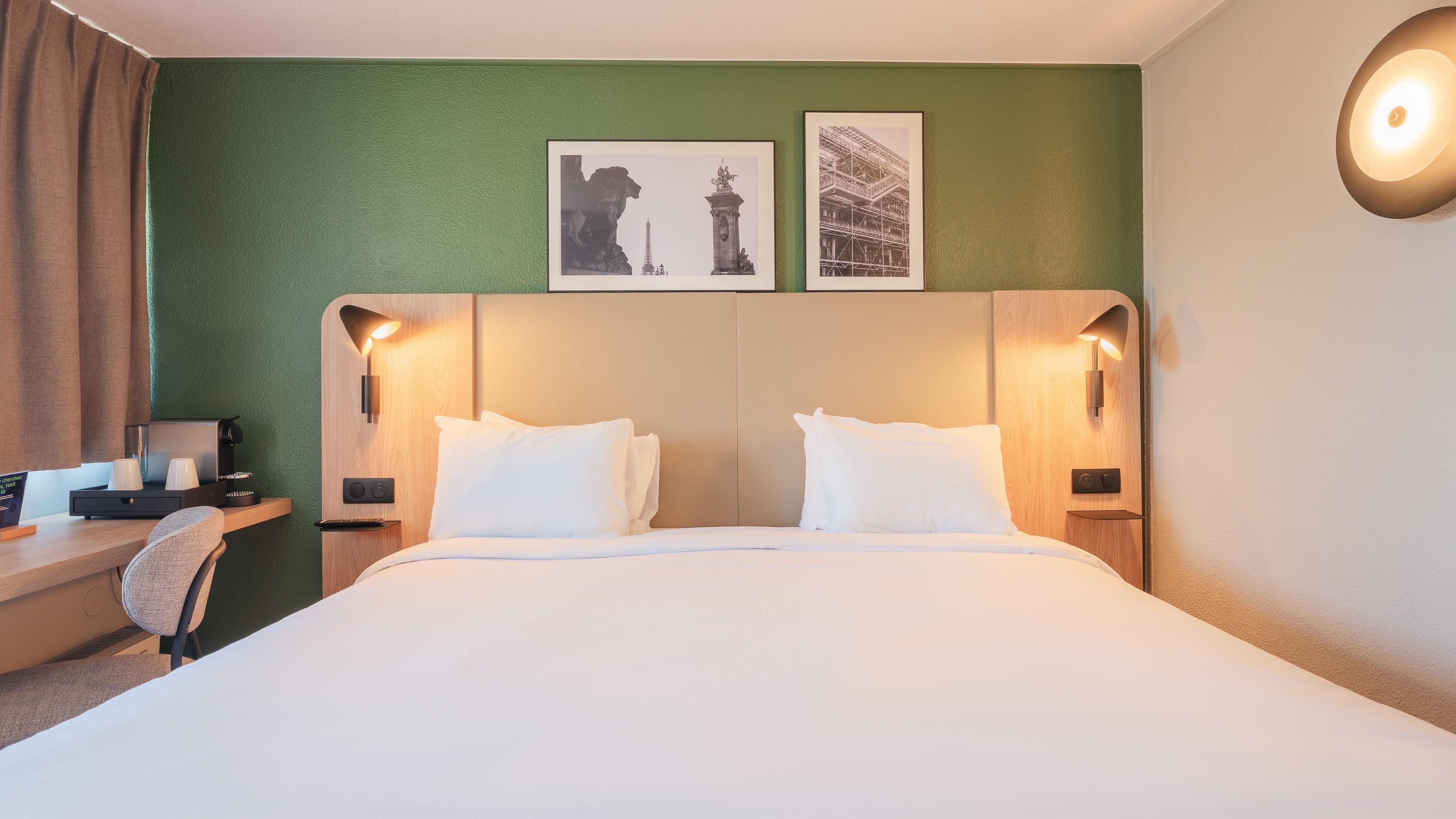 Habitación de hotel con una cama grande, dos lámparas de pared, un escritorio con silla y dos cuadros en la pared.