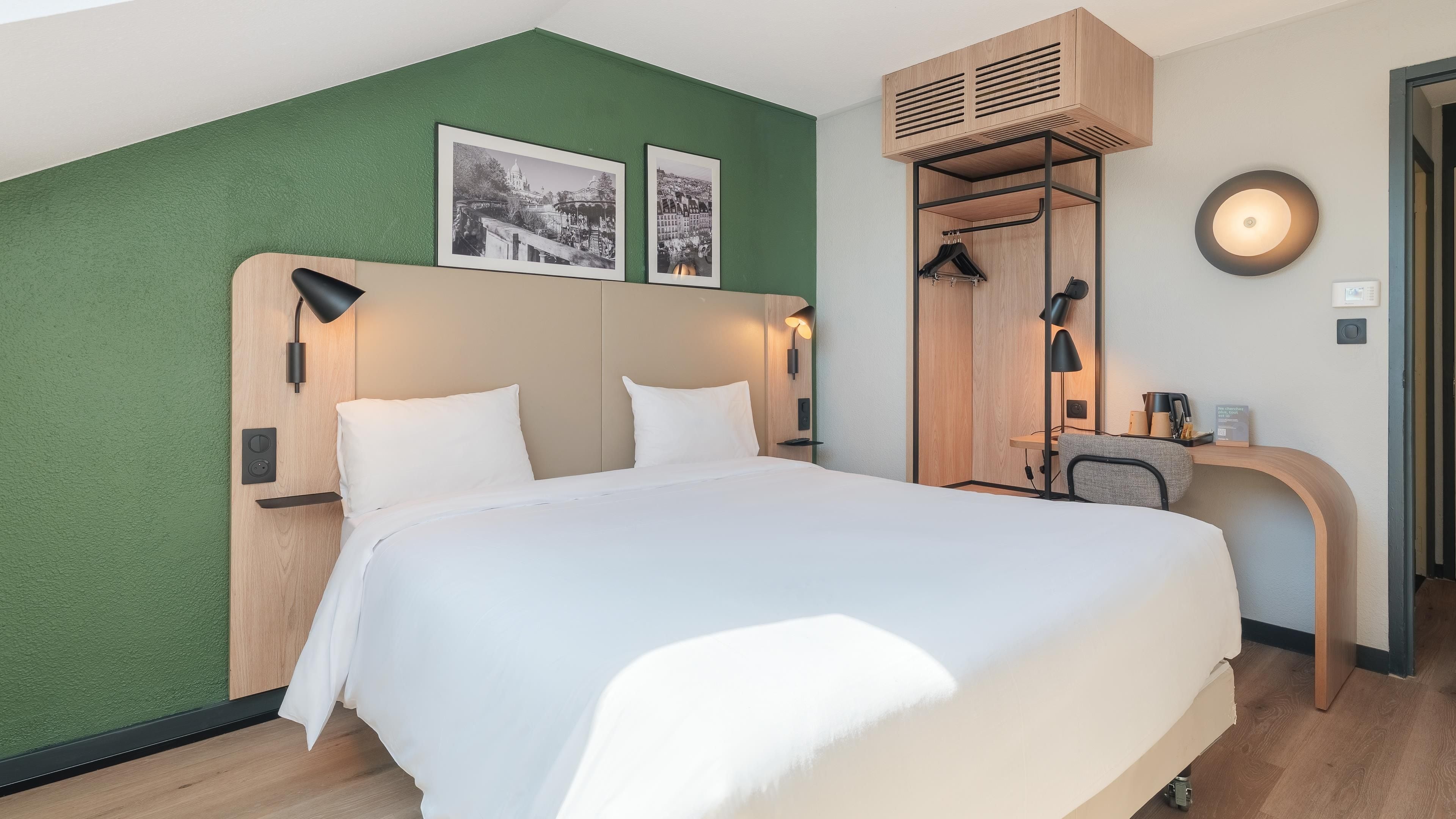 Quarto de hotel com cama, escrivaninha, espelho e parede verde.