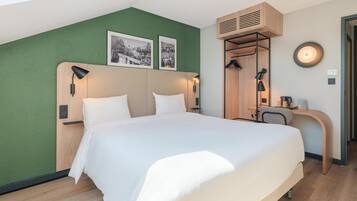 Quarto de hotel com cama, escrivaninha, espelho e parede verde.