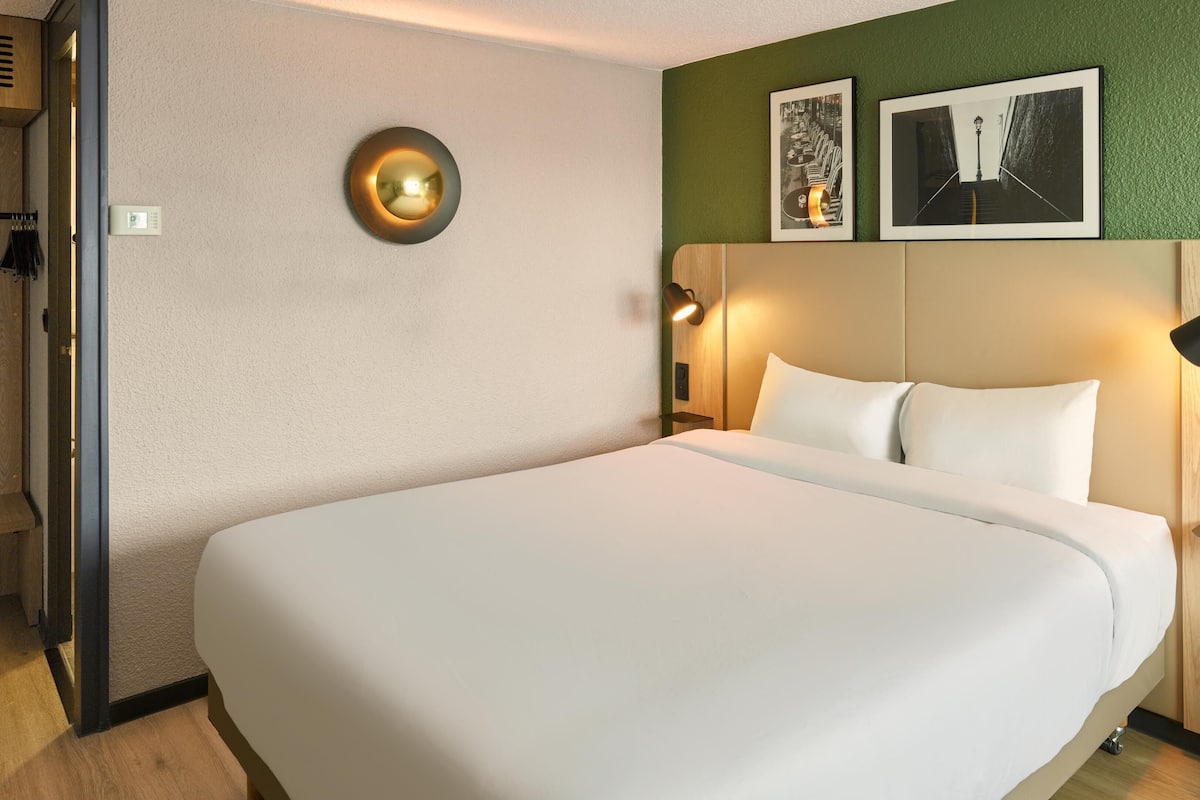 Ein Hotelzimmer mit einem großen Bett, einem Holzkopfteil, zwei Wandleuchten und zwei gerahmten Bildern an der Wand.